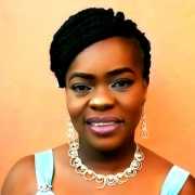 Portrait of a smiling woman with braided updo hair, an ornate silver necklace, and a light blue dress.